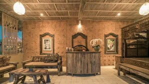 Un interior rústico con techo de madera, un banco central de madera, una mesita y un espejo decorativo.