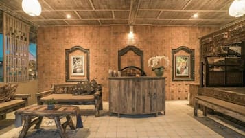 A rustic interior with a wooden ceiling, a central wooden bench, a small table, and a decorative mirror.