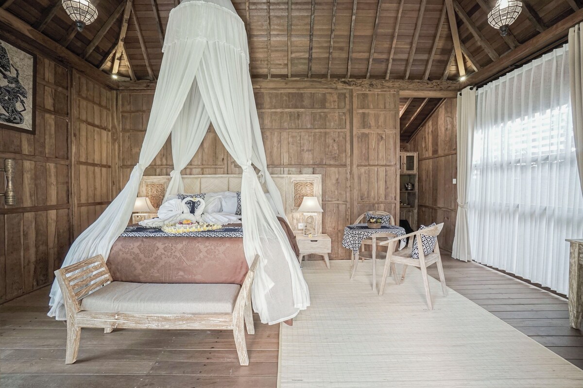 Une pièce rustique en bois, avec un lit à baldaquin, une chaise en bois, une petite table et une table de chevet.