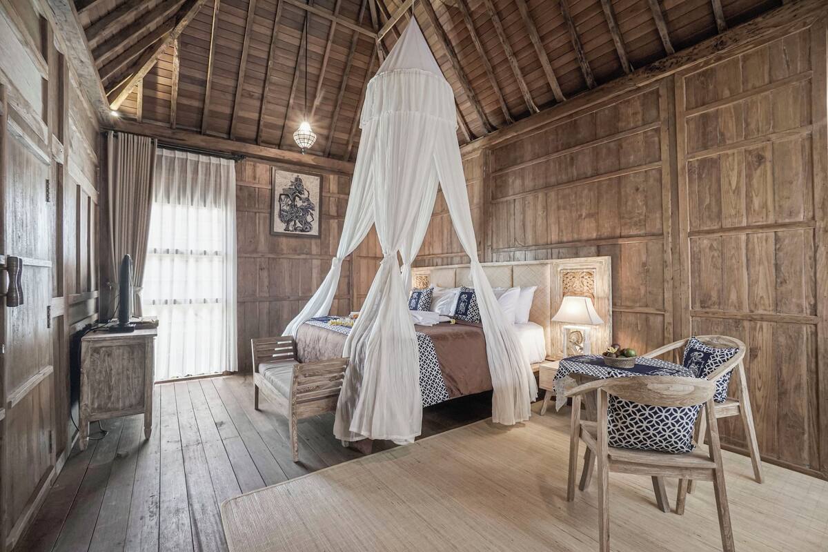 A rustic wooden room with a four-poster bed, a wooden bench, and a table with chairs.