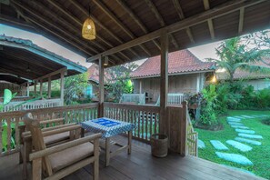 Eine Holzterrasse mit Tisch und Bänken, umgeben von einem Garten mit trittfesten Steinen und Blick auf traditionelle Häuser.