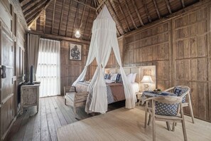 A rustic wooden room with a four-poster bed, a wooden bench, and a table with chairs. - Kirani Joglo (Celuk)