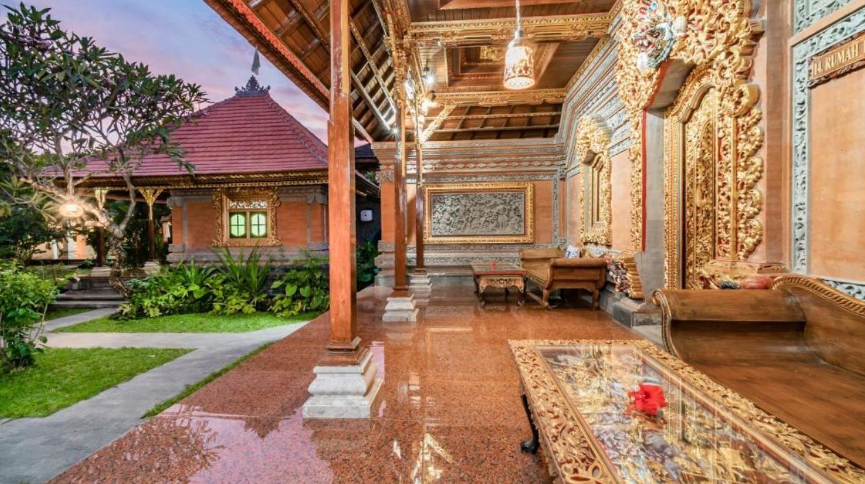 A traditional Balinese house with a wooden roof, a tiled floor, and a garden area.