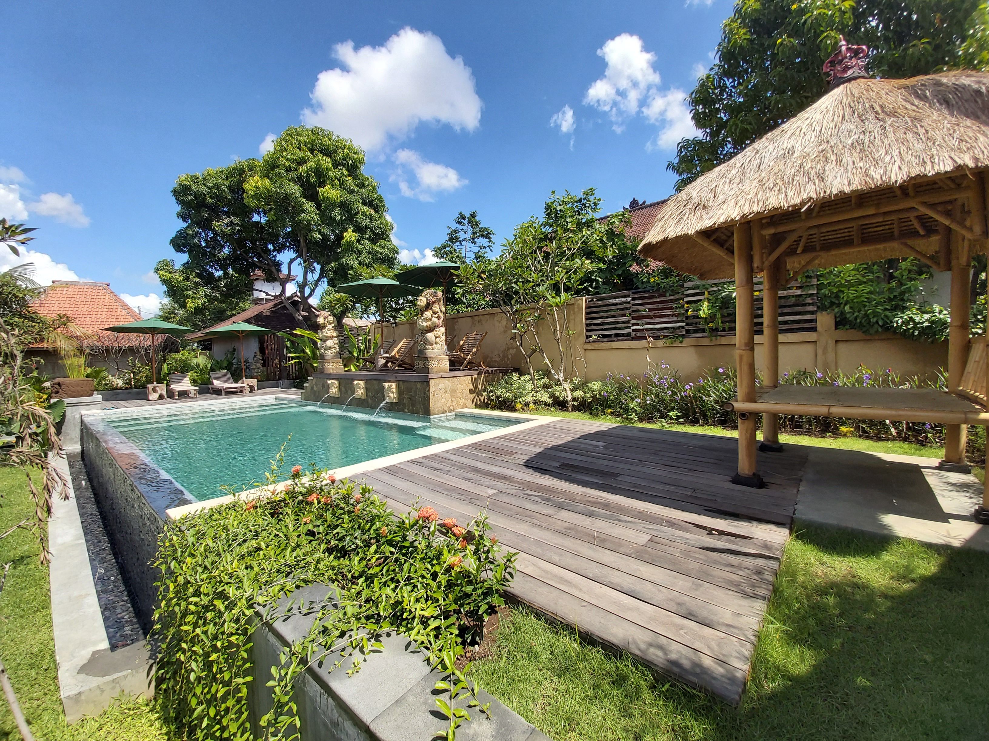 A swimming pool with a wooden deck, lounge chairs, and a thatched-roof gazebo.