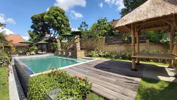 A swimming pool with a wooden deck, lounge chairs, and a thatched-roof gazebo.