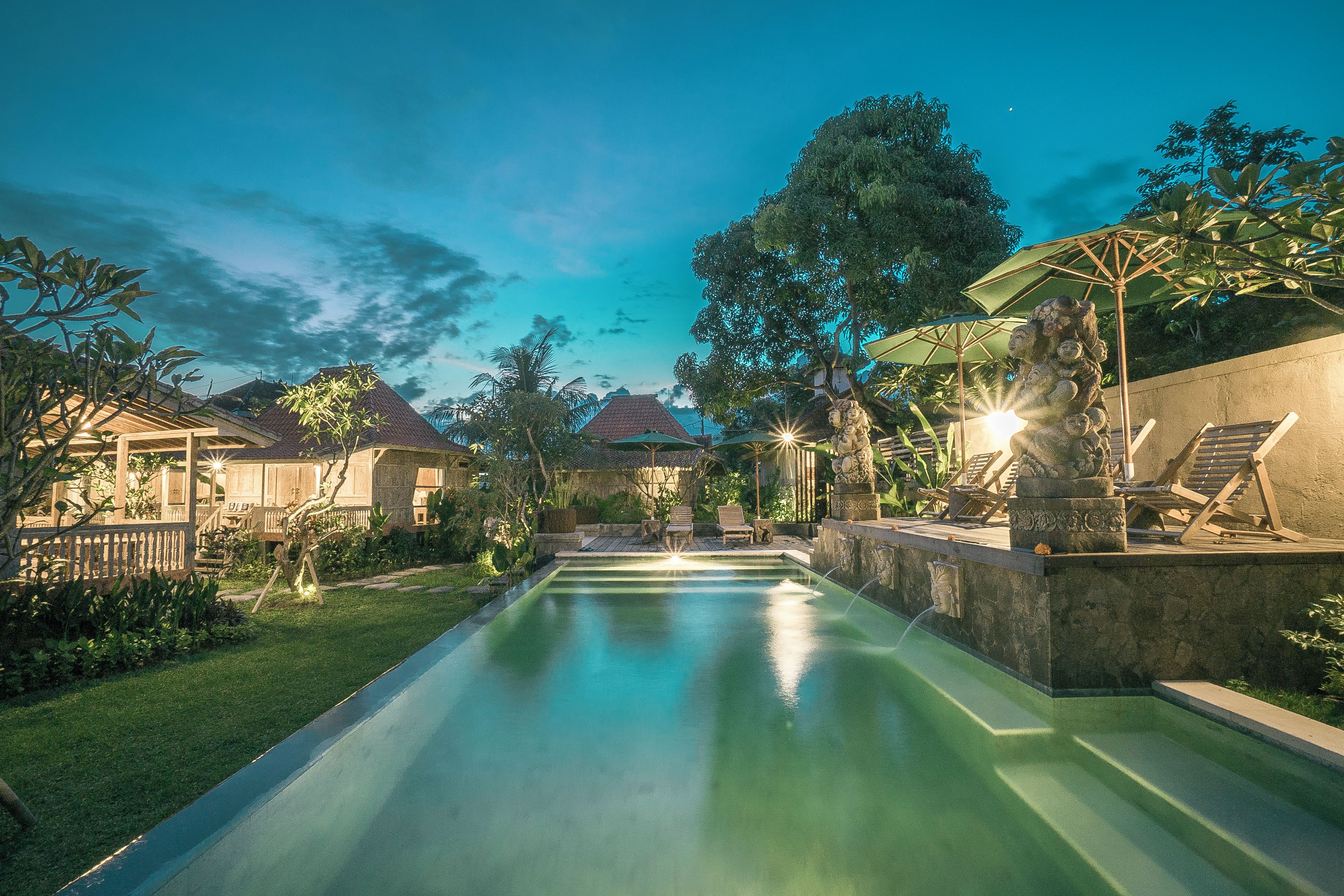 A swimming pool with lounge chairs and umbrellas, surrounded by greenery and a stone wall.