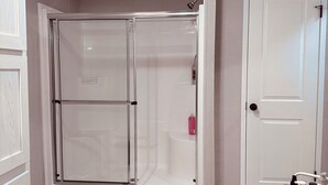 A bathroom with a glass shower enclosure, a white door, and a vanity with toiletries. - K & M Suite is a brand-new home in a peaceful, quiet neighborhood. (Wabash)