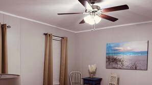 A bedroom with a bed, a ceiling fan, a painting of a beach, and two chairs. - K & M Suite is a brand-new home in a peaceful, quiet neighborhood. (Wabash)