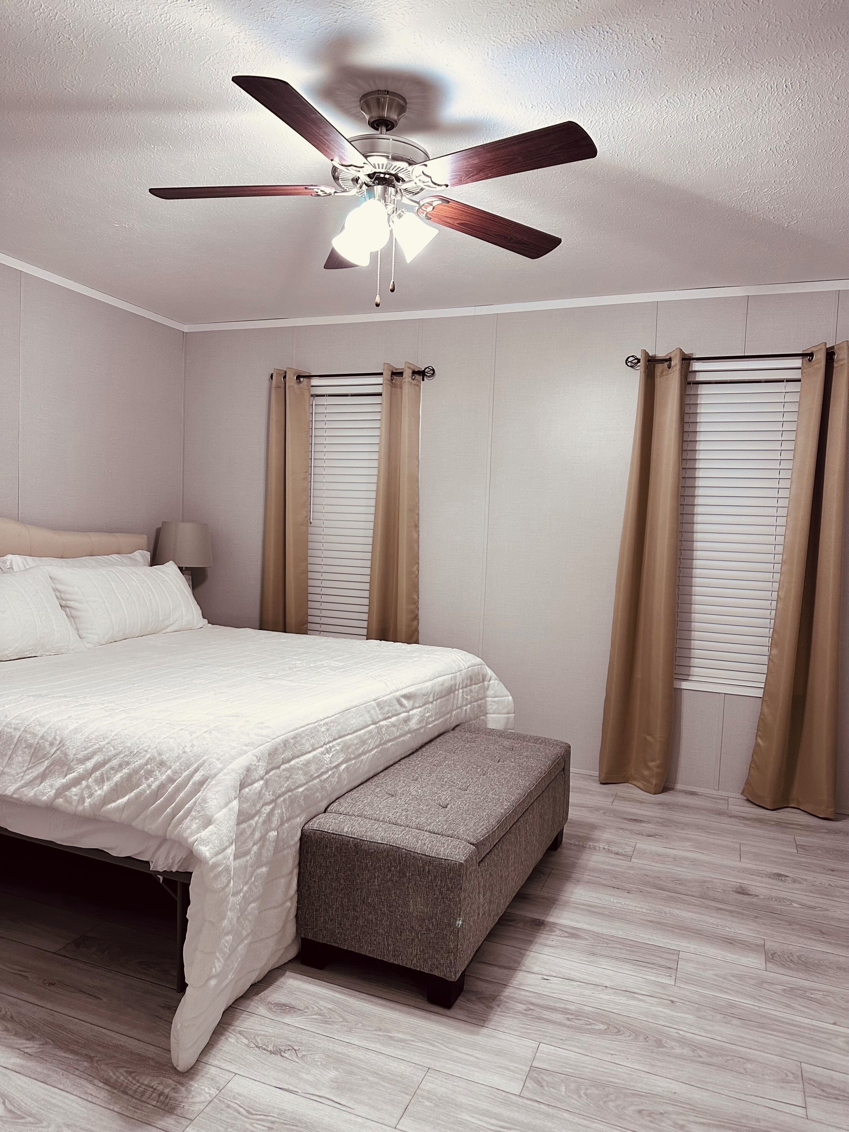 Quarto com uma cama, um banco, um ventilador de teto e cortinas.