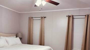 Quarto com uma cama, um banco, um ventilador de teto e cortinas.