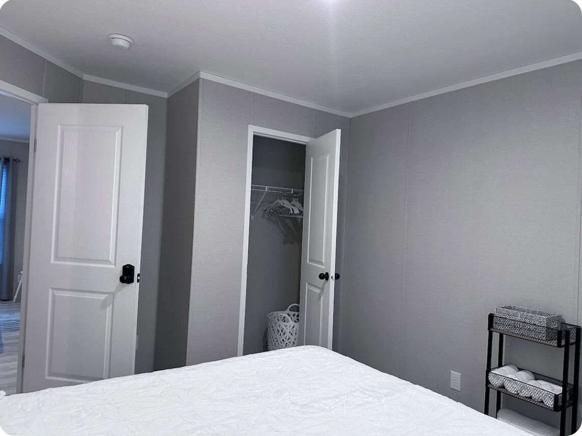 A bedroom with a bed, a white door, a closet, and a small shelf.