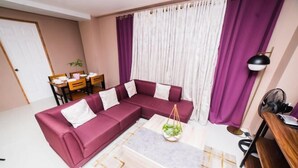 Una sala de estar con un sofá modular, una mesa de centro, una mesa de comedor con sillas y una lámpara.