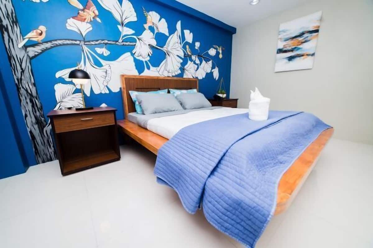 A bedroom with a bed, a nightstand, a lamp, a wall mural, and a painting.