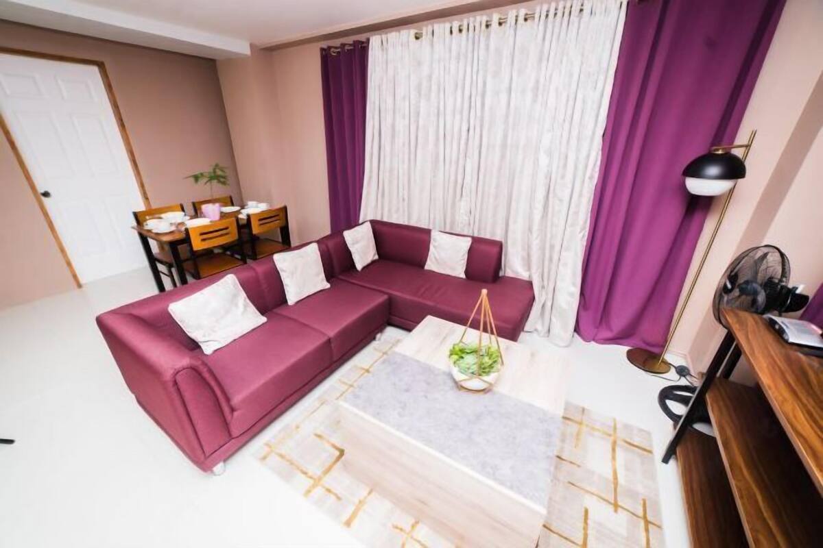 Una sala de estar con un sofá modular, una mesa de centro, una mesa de comedor con sillas y una lámpara.