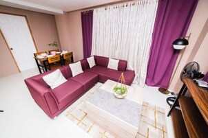 Una sala de estar con un sofá modular, una mesa de centro, una mesa de comedor con sillas y una lámpara.