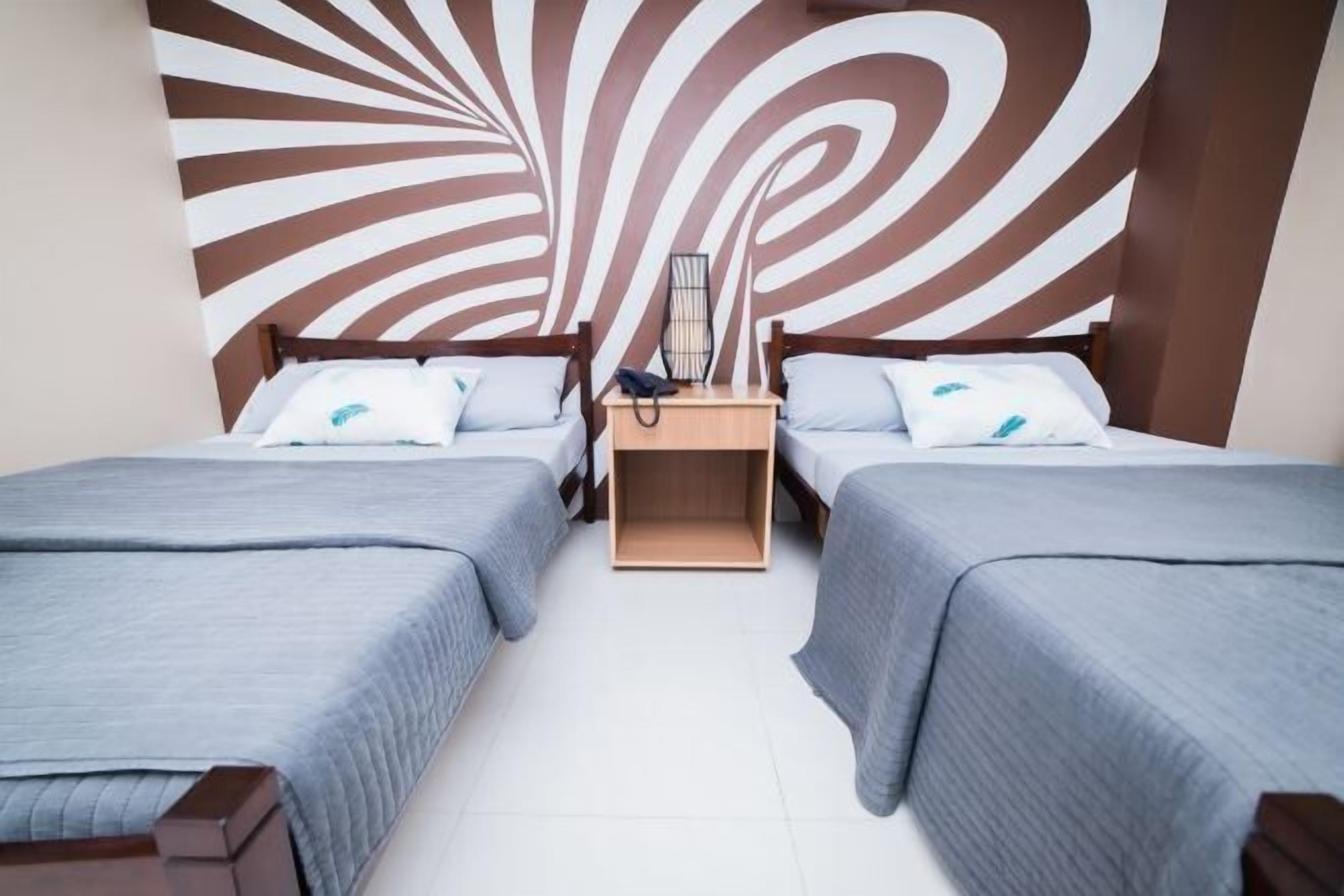 A room with two beds, a nightstand, and a wall with a spiral design.