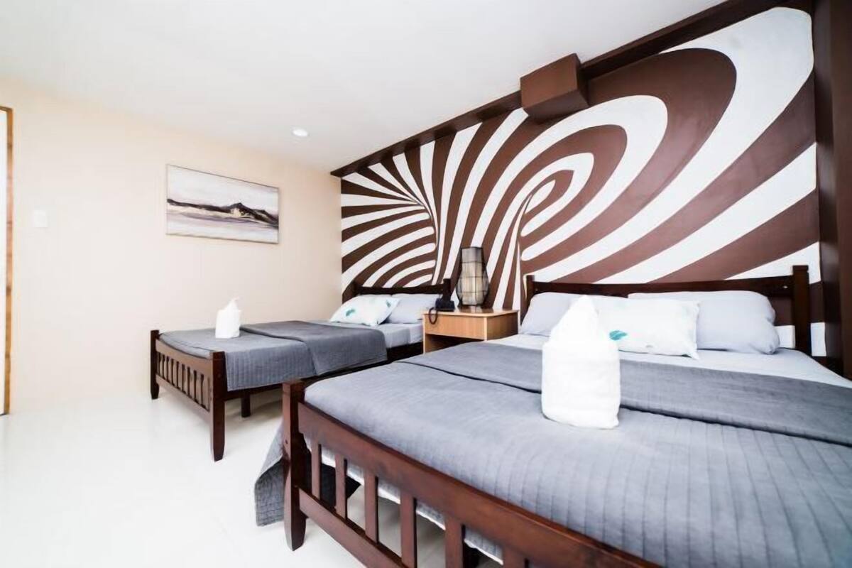 Habitación de hotel con dos camas, un diseño abstracto grande en la pared, una mesita de noche con una lámpara y un cuadro en la pared.