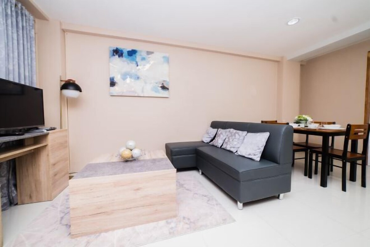 A modern living room with a sectional sofa, a flat-screen TV, a dining table with chairs, and a painting on the wall.