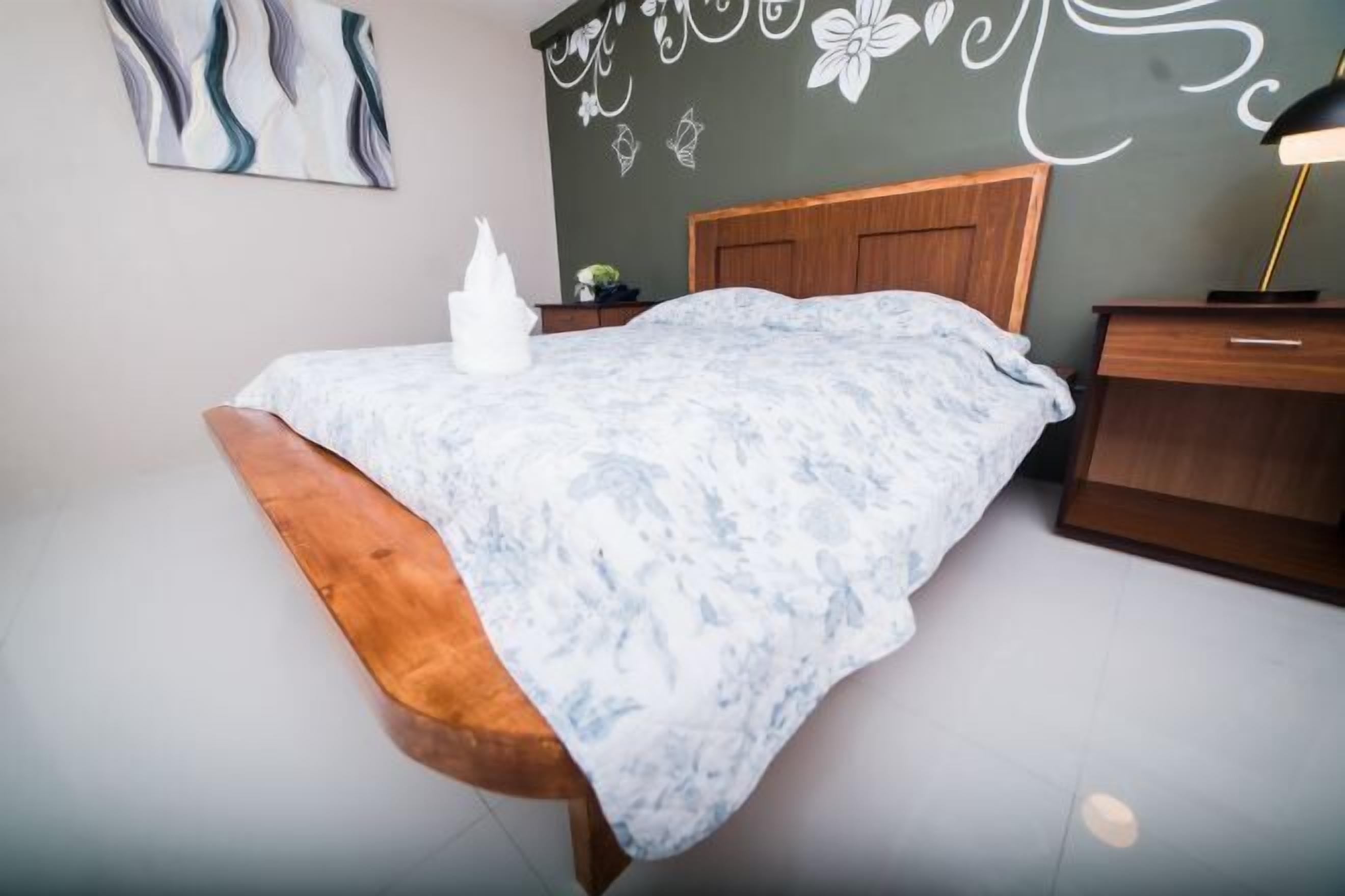 A bedroom with a bed, wooden headboard, bedside table, and a wall with floral decals.