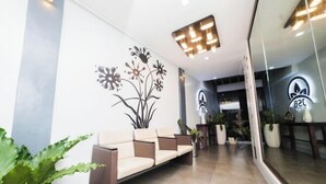 Un área de recepción con un sofá, plantas en macetas y una pared con diseño floral.