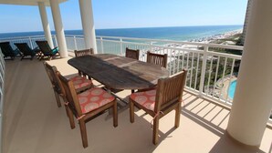 A balcony with a wooden table and chairs, overlooking a beach and a pool. - La Playa 703 (Pensacola)