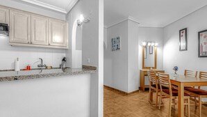 A modern kitchen with white cabinets and a granite countertop, a dining area with a wooden table and chairs, and a bathroom with a mirror and light fixture. - Apartment in Golf del Sur with heated pool (Golf del Sur)
