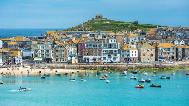 A coastal town with historic buildings, a hilltop structure, and a beach with boats. - Stunning iconic harbour & sea views of St Ives, parking and 2 mins walk to town (St Ives)