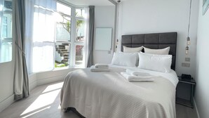 A modern bedroom with a large bed, a nightstand, and a window with curtains. - Stunning iconic harbour & sea views of St Ives, parking and 2 mins walk to town (St Ives)