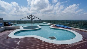 Une piscine sur le toit, dotée d’un design original, entourée d’une terrasse en bois et d’une rambarde en verre.
