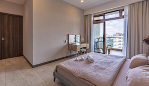 A hotel room with a large bed, a desk with a mirror, and a view of the city through the window.