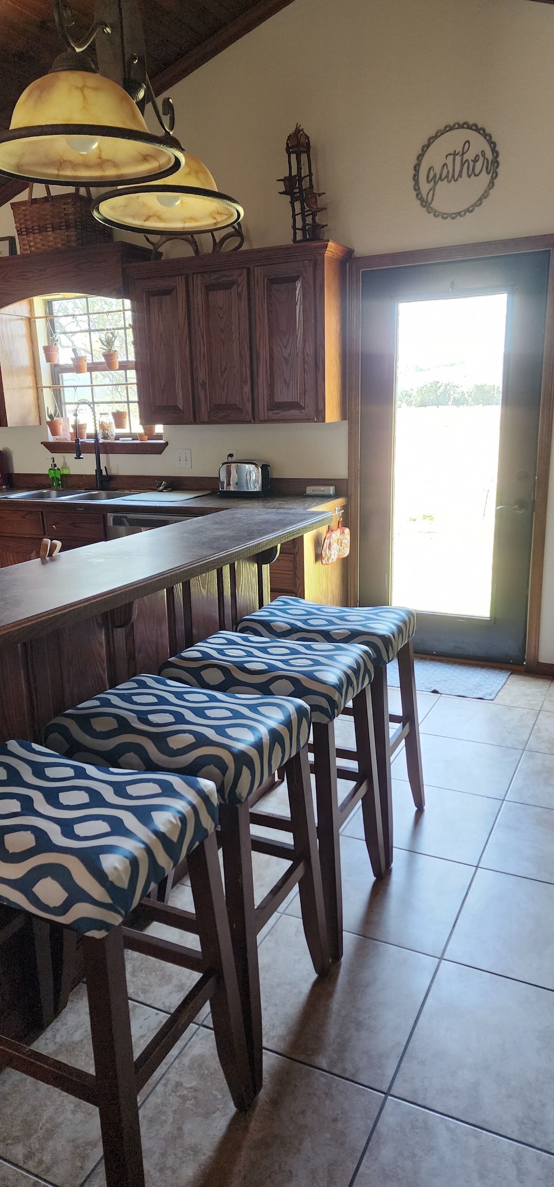 Une cuisine avec des meubles de rangement en bois, un îlot central intégré et un banc agrémenté de coussins à motifs.