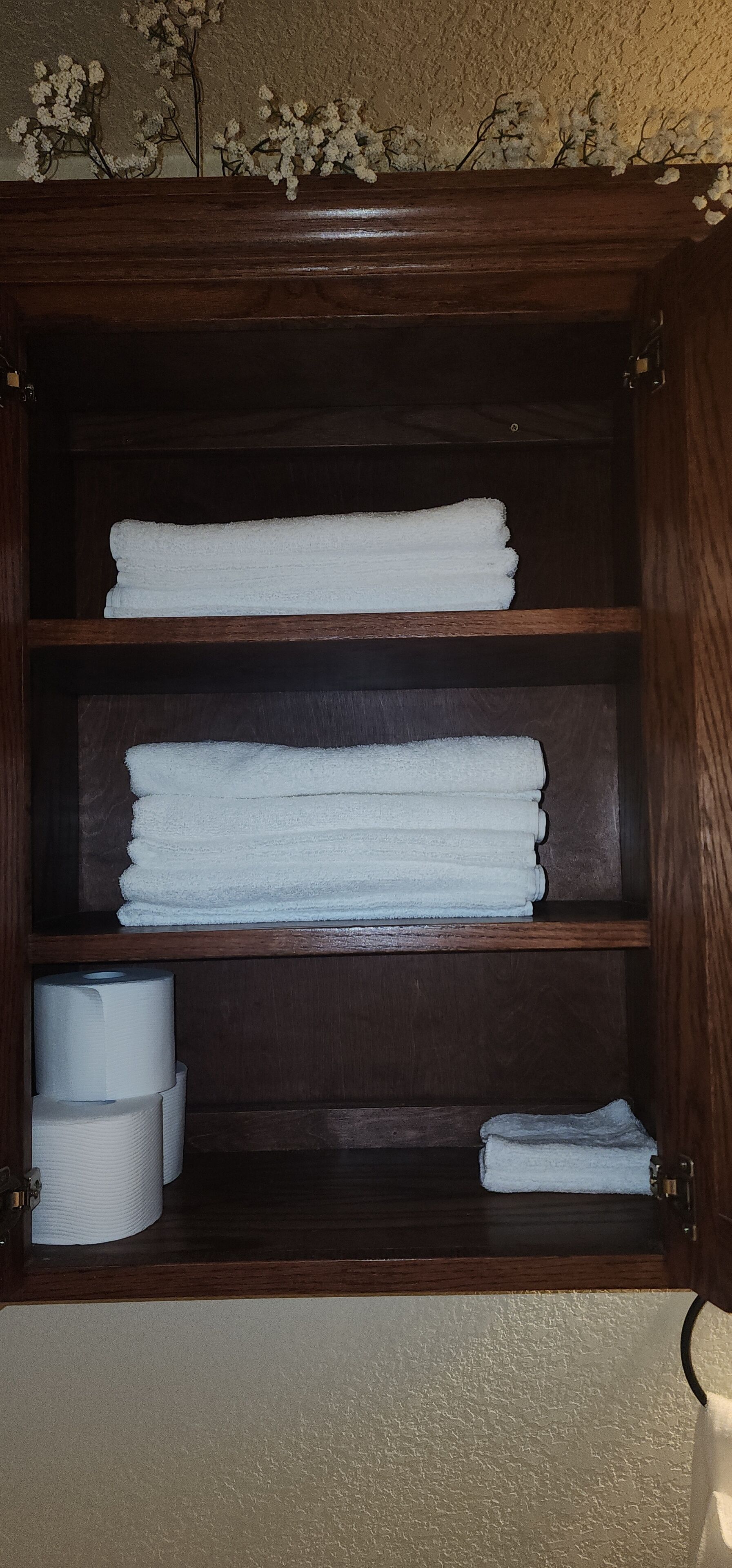 A wooden cabinet with three shelves, each holding neatly folded white towels.