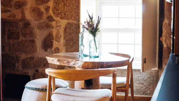 A rustic stone wall, a round wooden table with a glass vase and flowers, and a cushioned chair. - a cosy contemporary one-bedroom studio unit with 31 m2 (Sortelha)