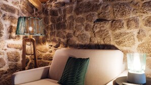 A stone-walled room with a beige armchair, a green pillow, a floor lamp, and a glass candle holder. - a cosy contemporary one-bedroom studio unit with 31 m2 (Sortelha)