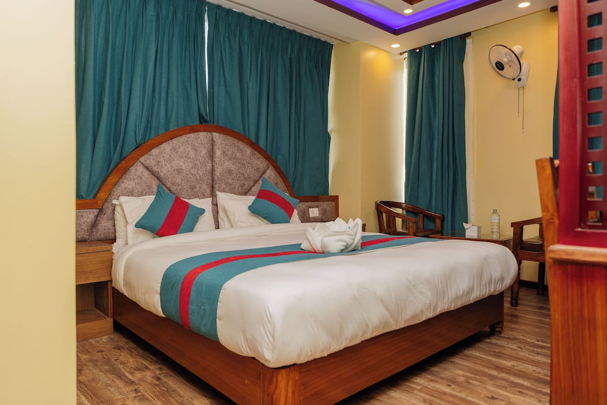 A hotel room with a large bed, wooden headboard, teal curtains, and a ceiling fan.