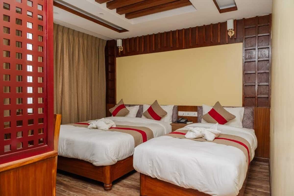A hotel room with two single beds, wooden headboards, a red lattice partition, and a beige curtain.