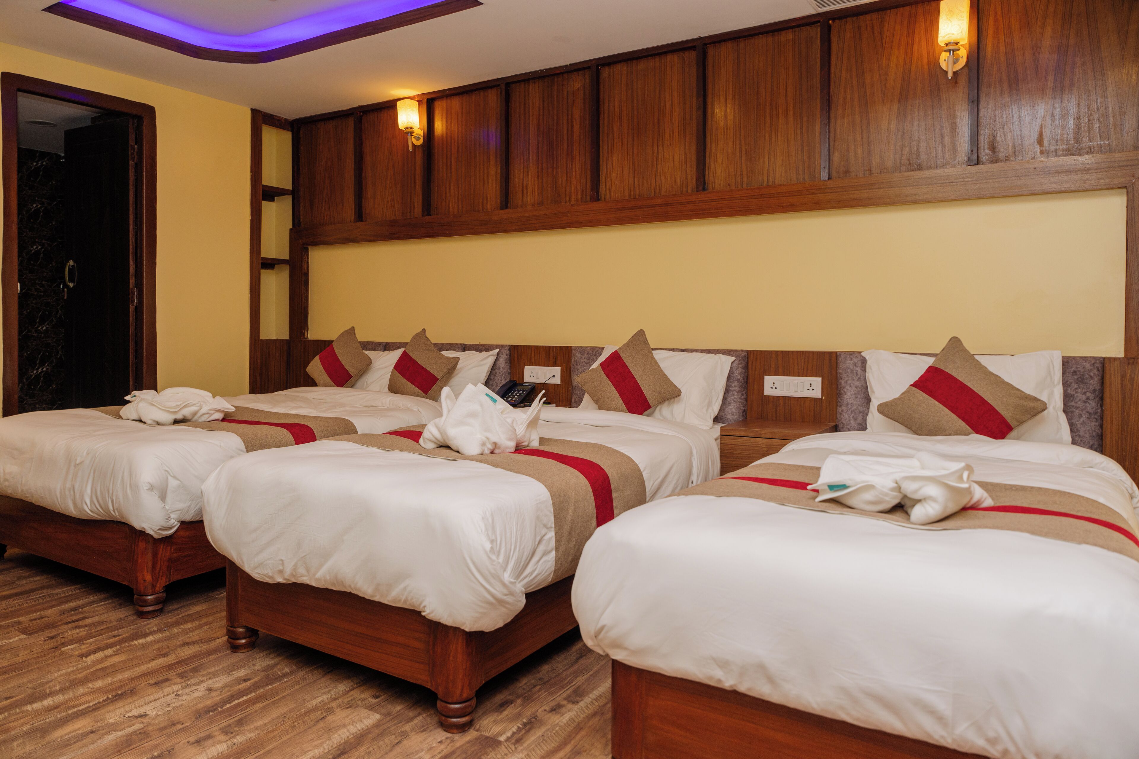 A hotel room with three wooden beds, each with white bedding and red and beige pillows.