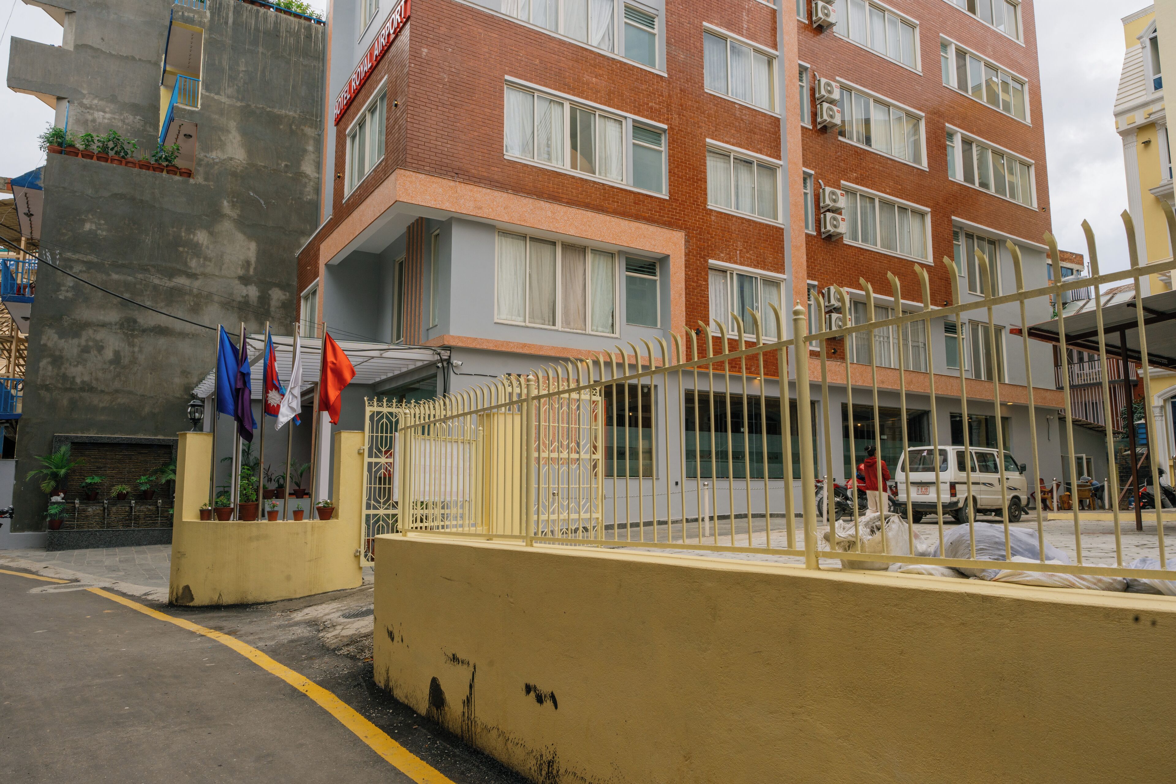 Ein mehrstöckiges Hotel mit gelber Fassade, einem verschlossenen Eingangsbereich und Pflanzen in Töpfen vor dem Eingang.