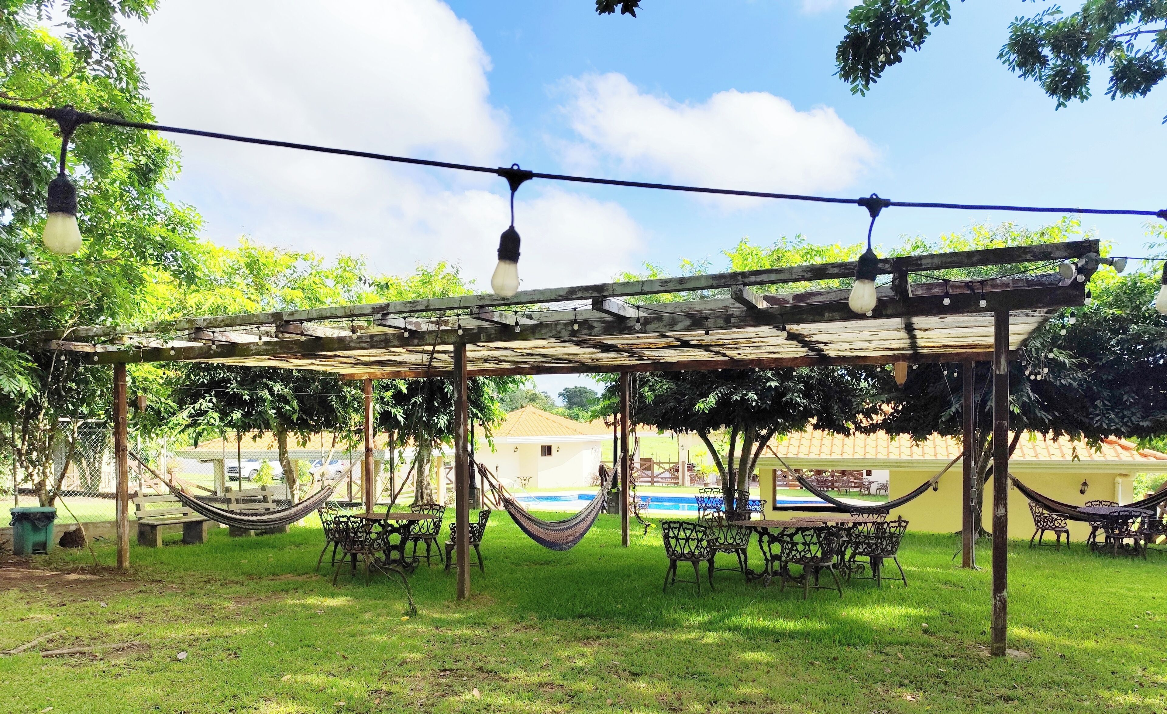 A covered outdoor seating area with tables and chairs, a hammock, and string lights.
