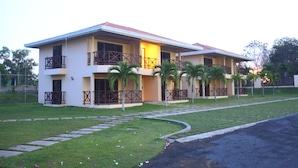 A two-story building with balconies, a paved driveway, and a lawn with scattered flowers. - Pocri Country Resort  (Pocrí)