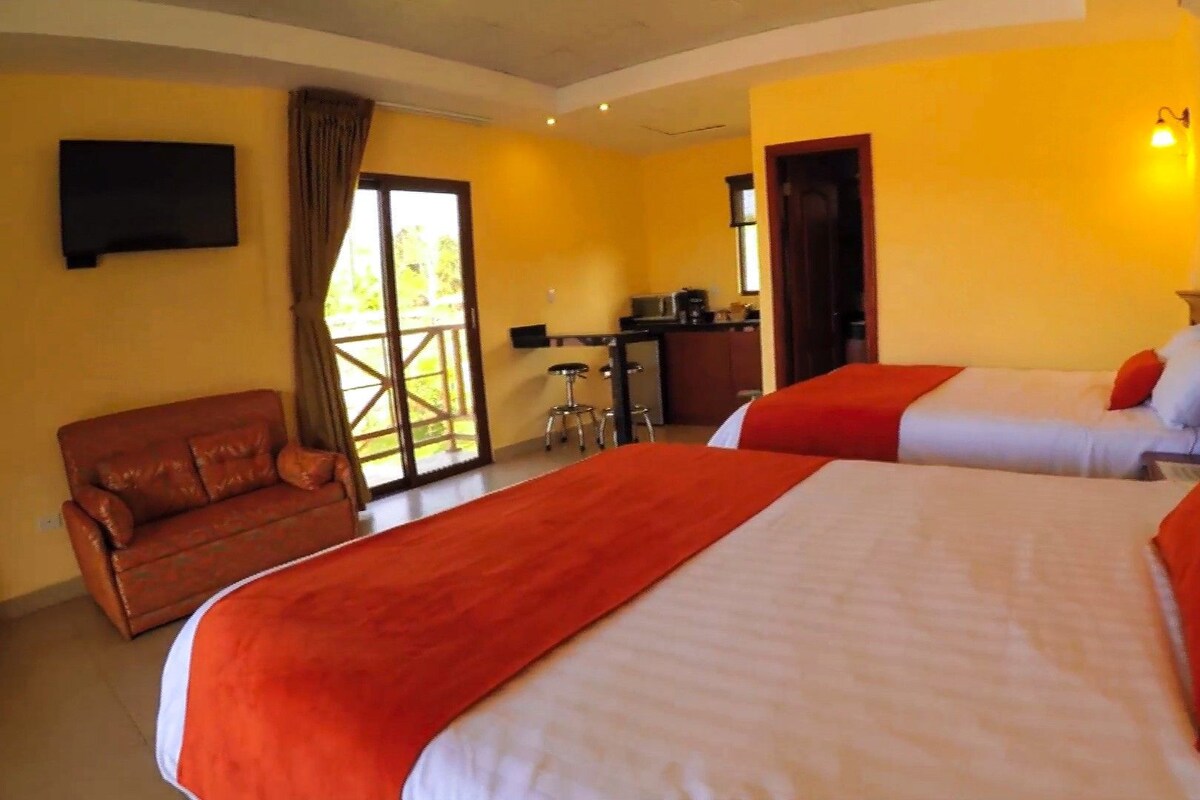 A hotel room with two beds, a sofa, a desk, and a view of the outdoors.