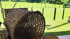 A wicker basket filled with hay on a table, with a view of a green field and trees in the background. - Pocri Country Resort  (Pocrí)