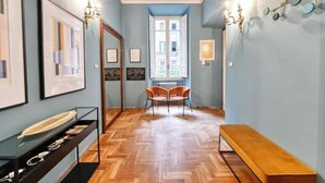 A hallway with a wooden parquet floor, framed artwork on the walls, a bench, and a table with a display of items. - Elegant Historic Apartment in Central Rome
 (Roma)