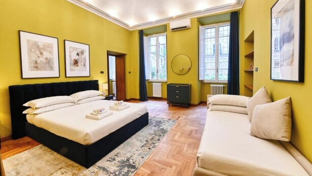 A room with a large bed, a sofa, and two windows with curtains. - Elegant Historic Apartment in Central Rome
 (Roma)
