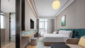Une chambre d’hôtel moderne dotée d’un grand lit, d’un canapé, d’une petite table, d’une télévision et d’un balcon avec des rideaux.