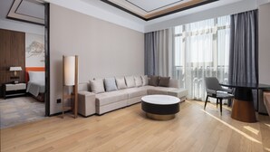 Une chambre d’hôtel moderne, dotée d’un canapé, d’une table basse ronde, d’une table à manger et offrant une vue sur la ville grâce à de grandes fenêtres.