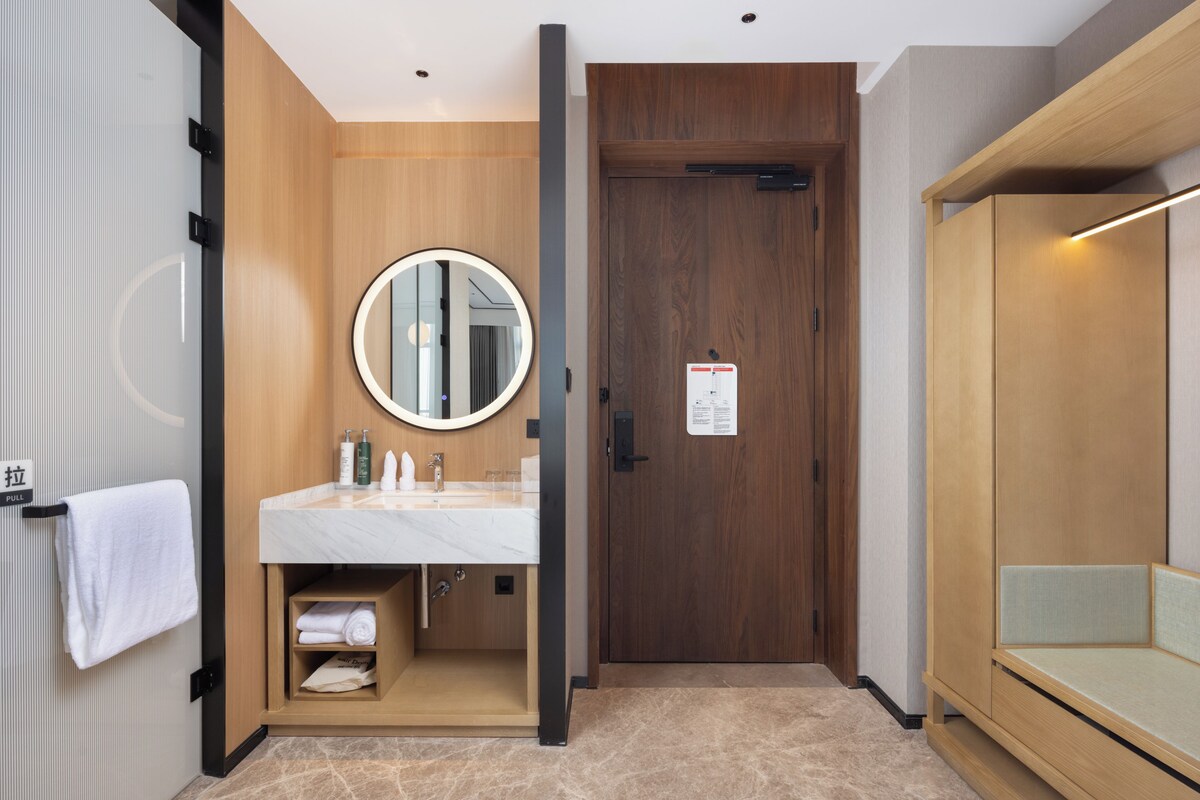 Een moderne badkamer met een houten wastafelmeubel, een ronde spiegel en een bankje.