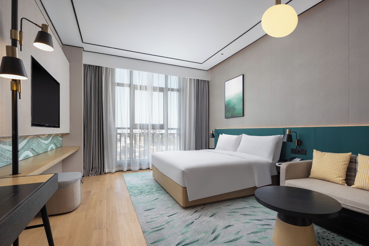 Ein modernes Hotelzimmer mit Bett, Sofa, Schreibtisch und Fernseher.