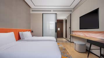 A modern hotel room with two beds, a desk, a television, and a waste bin.