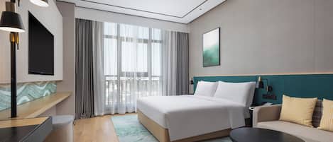 A modern hotel room with a bed, a sofa, a desk, and a TV.